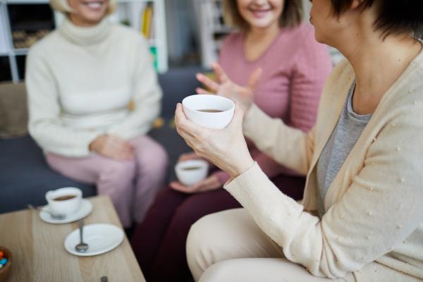 Group of three unrecognisable women chatting over hot drinks in cups