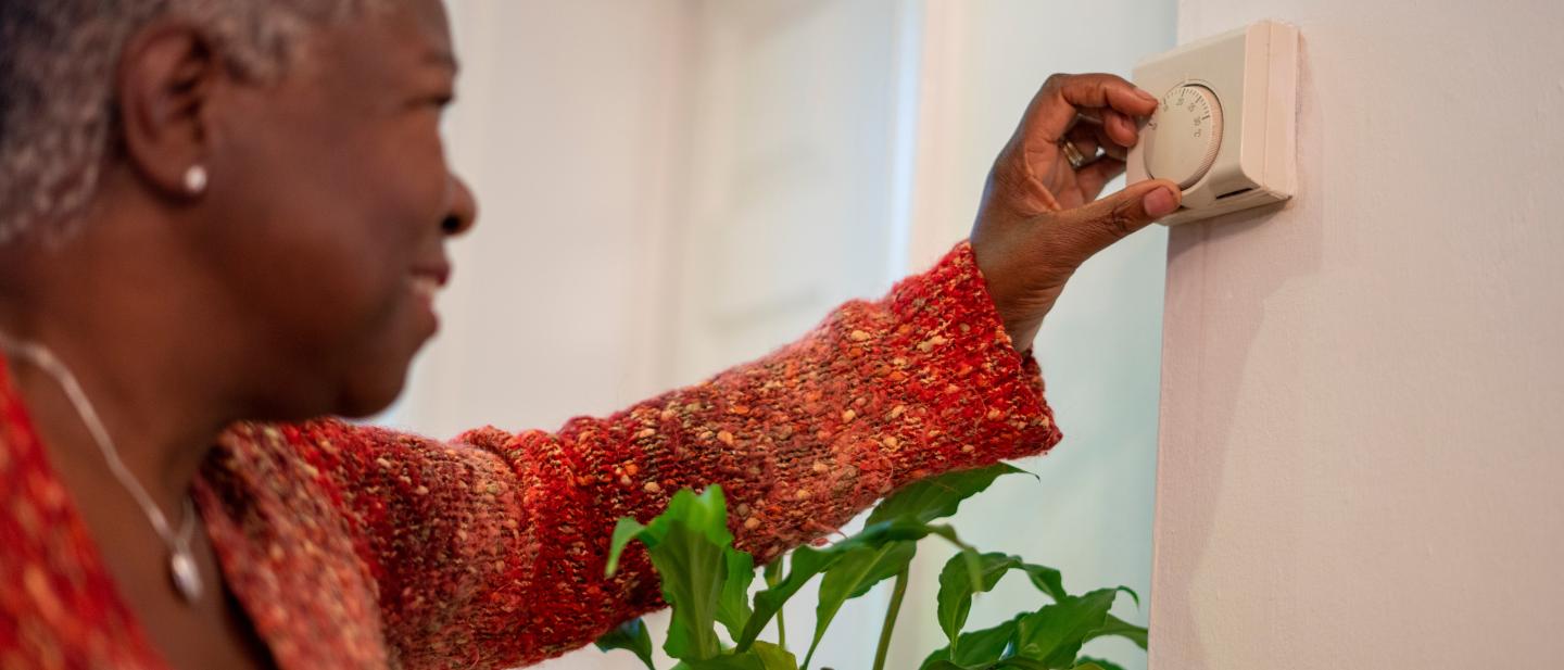 Lady in a red top adjusting a heating thermostat on a wall.